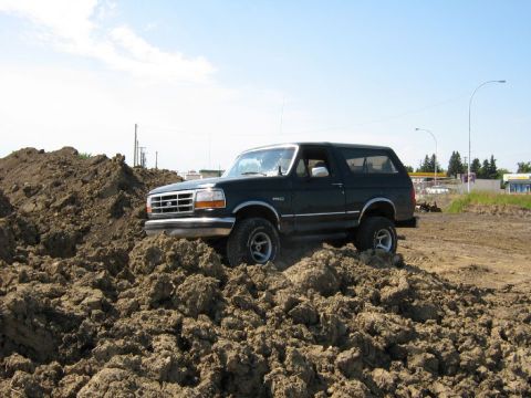 1995 Ford Bronco - Dark green Ford Bronco navigates a mound of dirt under a clear sky.