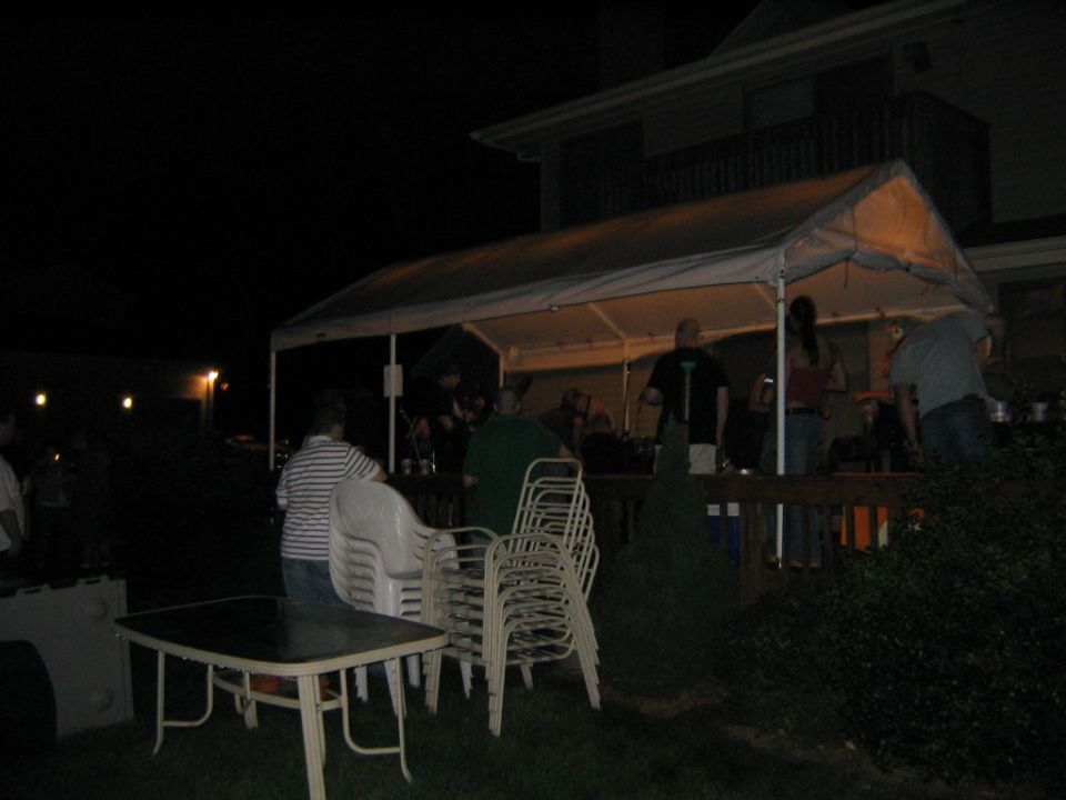 people gathered under a tent at night, with tables and chairs set up