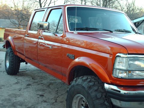 1991 Ford F-350 - This orange Ford F-350 pickup truck features a four-door cab and appears to have a lifted suspension with large off-road tires.