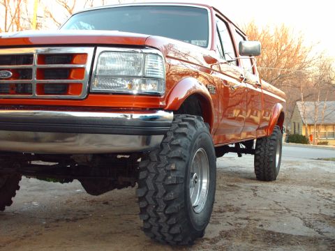 1991 Ford F-350 - This orange 1991 Ford F-350 pickup truck is shown from a front 3/4 angle, highlighting its large off-road tires.