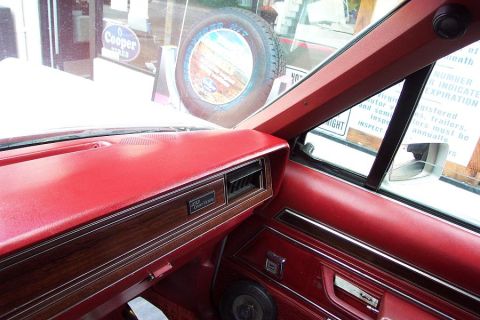 1985 Ford LTD Crown Victoria - Interior shot from the driver's side of a red-upholstered Ford Crown Victoria, looking across the padded red dash with woodgrain trim, a 'C…