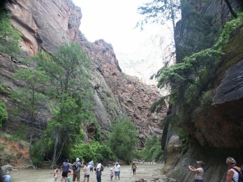 2001 Mercury Grand Marquis - A group of people are seen walking through a river in a canyon, with towering rock formations on either side.