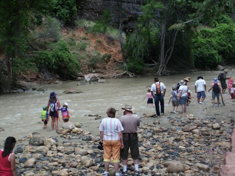 2001 Mercury Grand Marquis - A group of people, including children, are seen wading through a river in a natural setting with rocky shores and lush vegetation.