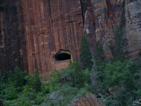 2001 Mercury Grand Marquis - A natural cave opening is visible in the side of a large, striated red rock cliff, surrounded by green trees and vegetation.