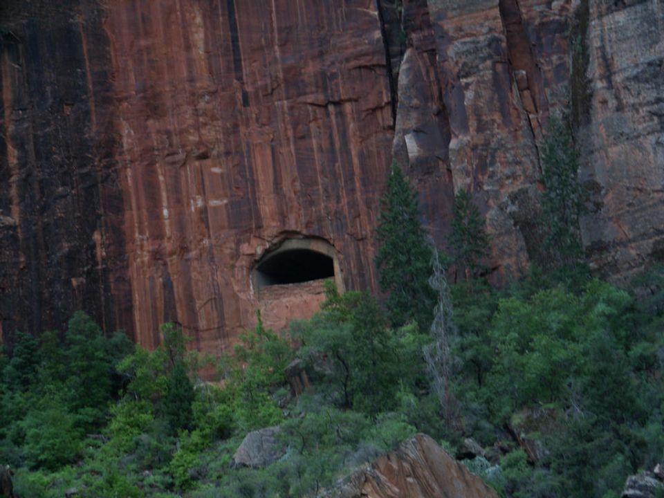 Cave entrance in a red rock cliff face with trees and foliage