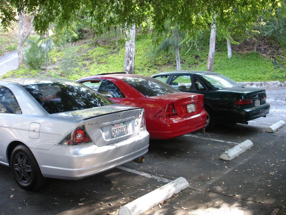 Three sedans parked in a lot, two in foreground, one in background