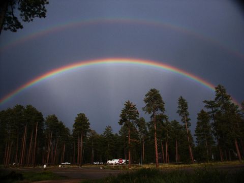 2001 Mercury Grand Marquis - A double rainbow appears in a dark sky above a forest, with a campground and several vehicles in the background.