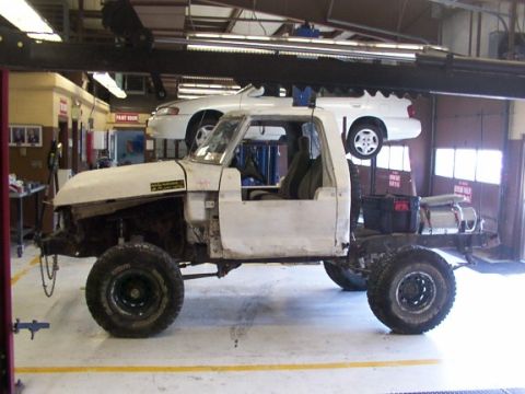 1978 Ford Bronco - A white pickup truck chassis is being worked on in a garage, with another vehicle suspended above it.