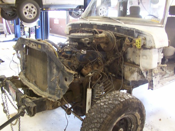 Disassembled vehicle front end with engine exposed, on a lift