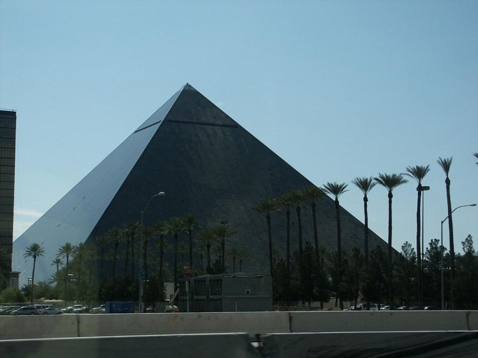Pyramid-shaped hotel with palm trees and a tall building next to it