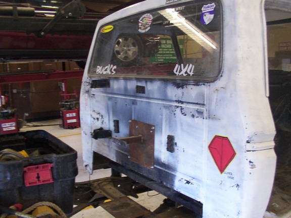Rear of white vehicle with "BUCKS" and "4x4" stickers, spare tire visible inside