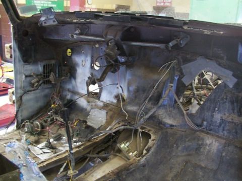 1978 Ford Bronco - The interior of a vehicle is shown in a state of disassembly, revealing exposed wiring and rusted metal components.
