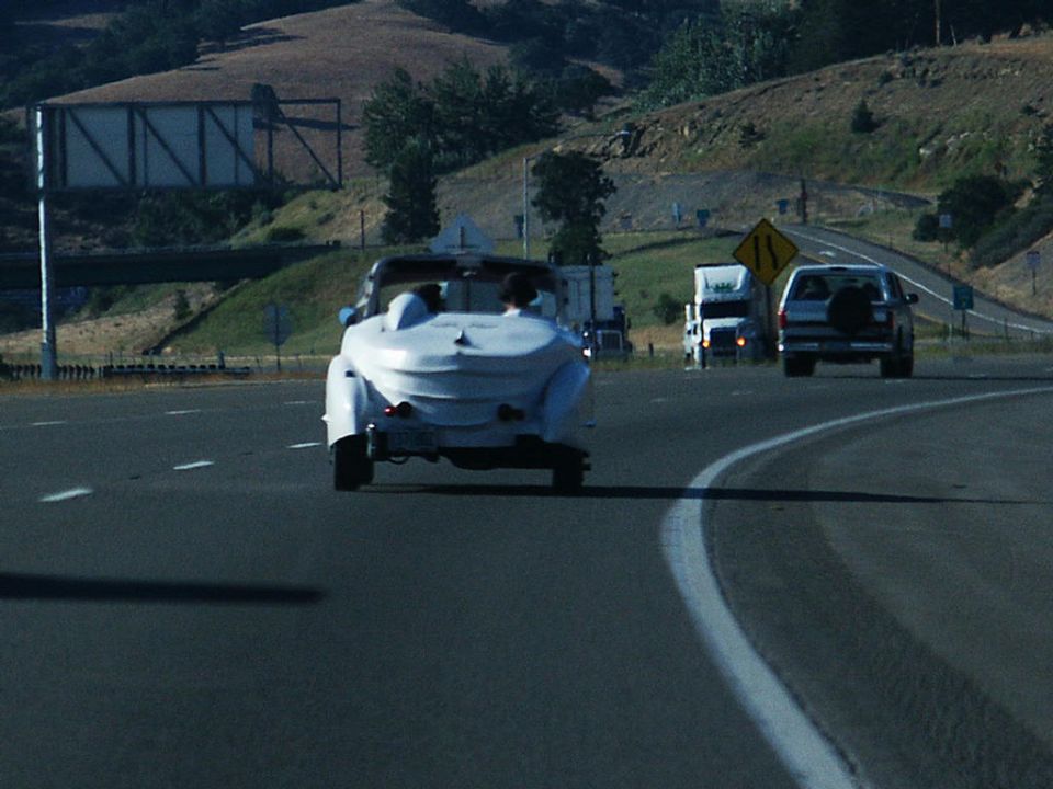 Custom white convertible with two people driving on a highway, other vehicles in background