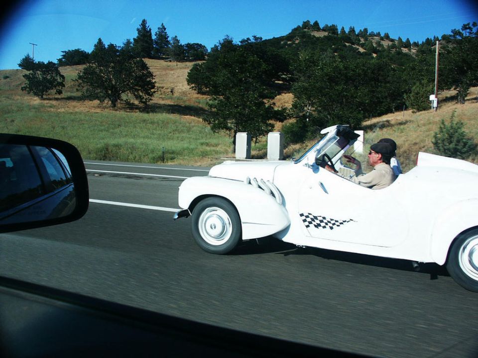 White convertible with checkerboard decal on the side driving on a highway