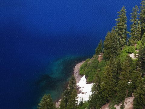 2001 Mercury Grand Marquis - A vast expanse of deep blue water meets a rocky shoreline dotted with evergreen trees and lingering snow.