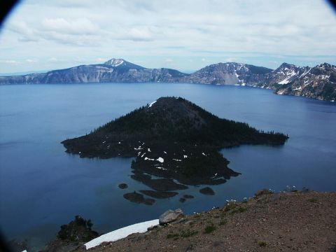 2001 Mercury Grand Marquis - A scenic view of Crater Lake, Wizard Island and snow-capped mountains under a cloudy sky.