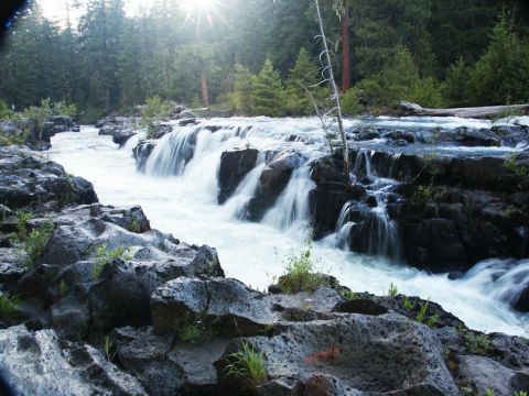 2001 Mercury Grand Marquis - A scenic view of a waterfall flowing over dark rocks, surrounded by lush green trees and a bright sunburst.