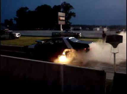 2001 Mercury Grand Marquis - A drag car performs a burnout, kicking up smoke and flames at dusk.