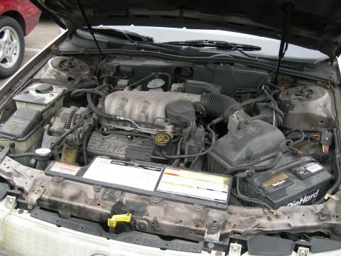 1992 Ford Taurus - The engine bay of a car is shown, with a V6 engine and a DieHard battery. Another vehicle is partially visible.