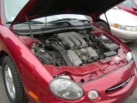 1992 Ford Taurus - The engine bay of a red 1992 Ford Taurus is visible, with another car parked behind it.