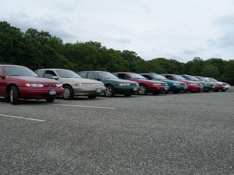 1992 Ford Taurus - Several sedans, including a 1992 Ford Taurus, are parked in a lot on a cloudy day.