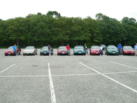 1992 Ford Taurus - A group of cars and people gathered in a parking lot with trees in the background.