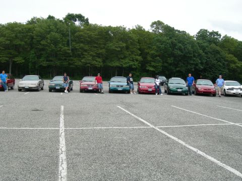 1992 Ford Taurus - A group of cars and people gathered in a parking lot on an overcast day.