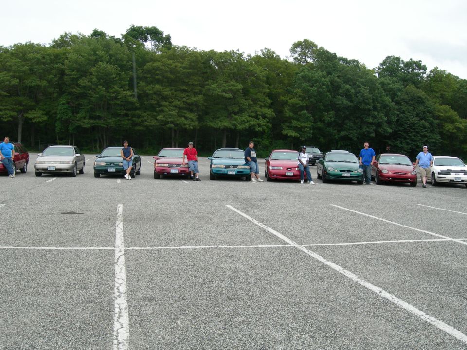 Several cars parked in a lot, including a 1992 Ford Taurus, with people standing around them