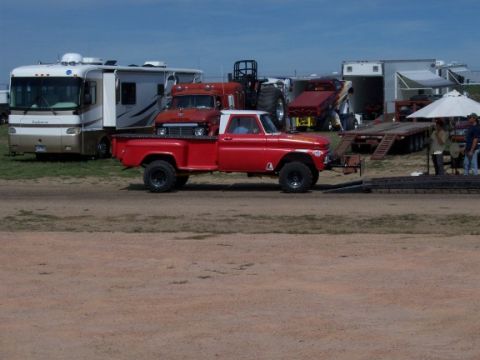 1972 Ford Ranchero - A red pickup truck with off-road tires is parked near a trailer, with an RV and other vehicles in the background.