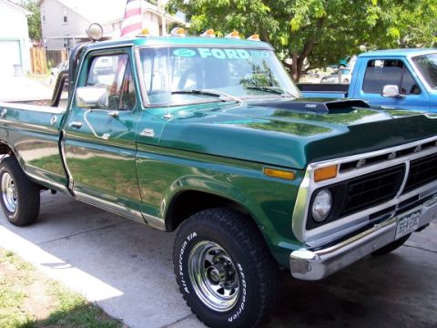 1972 Ford Ranchero - This green Ford pickup truck features a prominent chrome grille and a hood scoop, parked next to another truck.