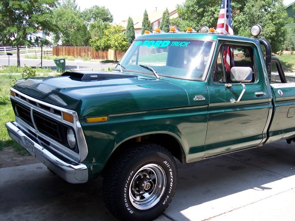 Green Ford pickup truck with a hood scoop and an American flag on the roof