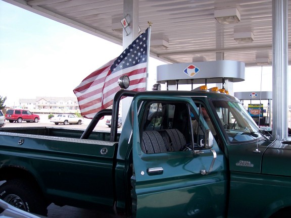 Green vintage pickup at gas pumps with roll bar, flag and diamond-plate bed rails