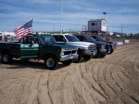 1972 Ford Ranchero - Several pickup trucks are lined up on a dirt track with a grandstand in the background.