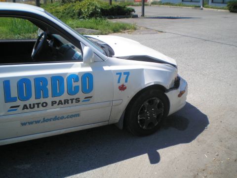 1985 Ford Bronco II - Damaged white sedan with 'LORDCO AUTO PARTS' branding and racing number 77.