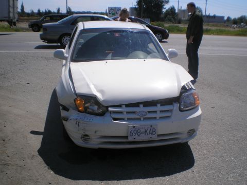 1985 Ford Bronco II - A white sedan sustained front-end damage after an apparent collision.