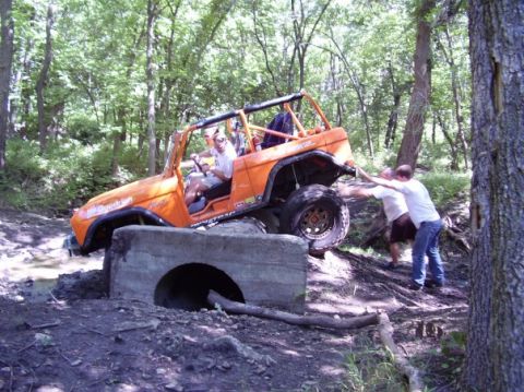 1994 Ford Bronco - An off-road vehicle navigates a challenging obstacle with assistance from bystanders.