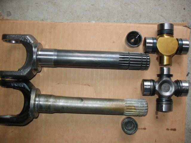 New and old axle shafts with new and used U-joints on cardboard
