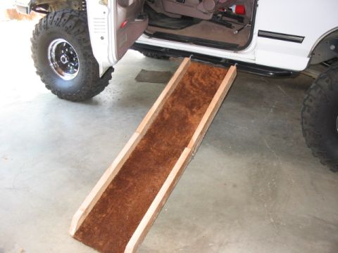 1995 Ford Bronco - A custom dog ramp is positioned next to a white 1995 Ford Bronco, highlighting its lifted suspension and large off-road tires.