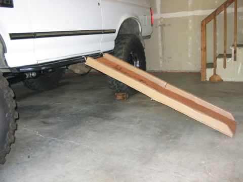 1995 Ford Bronco - A cardboard ramp is positioned next to the rear tire of a white SUV, likely for access.
