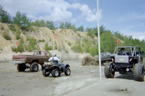2005 Dodge 1500 - Multiple off-road vehicles and an ATV are seen in a dirt area under a partly cloudy sky.