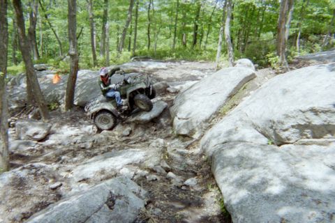 2005 Dodge 1500 - Rider maneuvers an ATV over large rocks on an off-road trail.