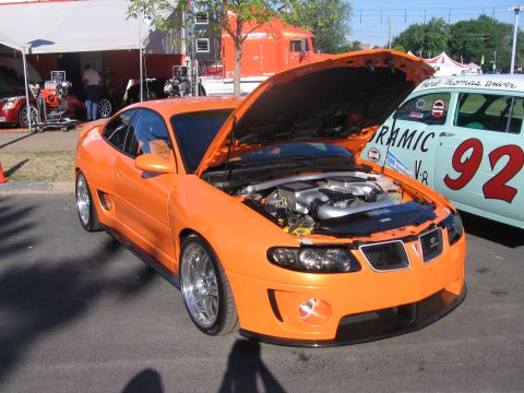 1989 Ford Mustang - An orange coupe with its hood open is parked next to a vintage race car.