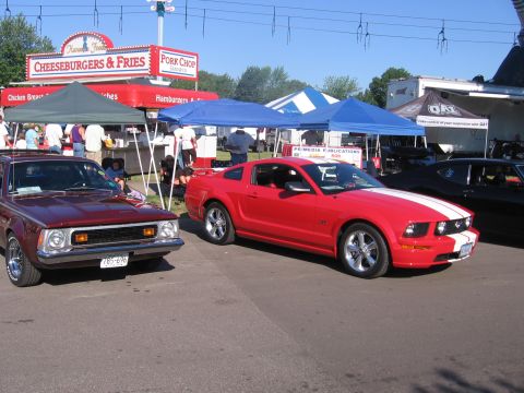1989 Ford Mustang - A red Ford Mustang with white stripes is parked next to a maroon car at an outdoor event with food vendors.