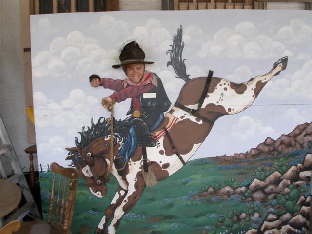 Person poking their face through a painted bucking-bronco cowboy photo cutout board