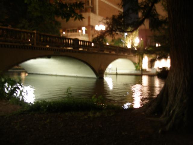 Stone arch bridge over the San Antonio River Walk lit at night with reflections on the water