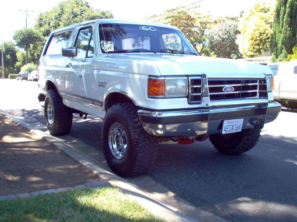 White 1990 Ford Bronco with chrome wheels and a brush guard