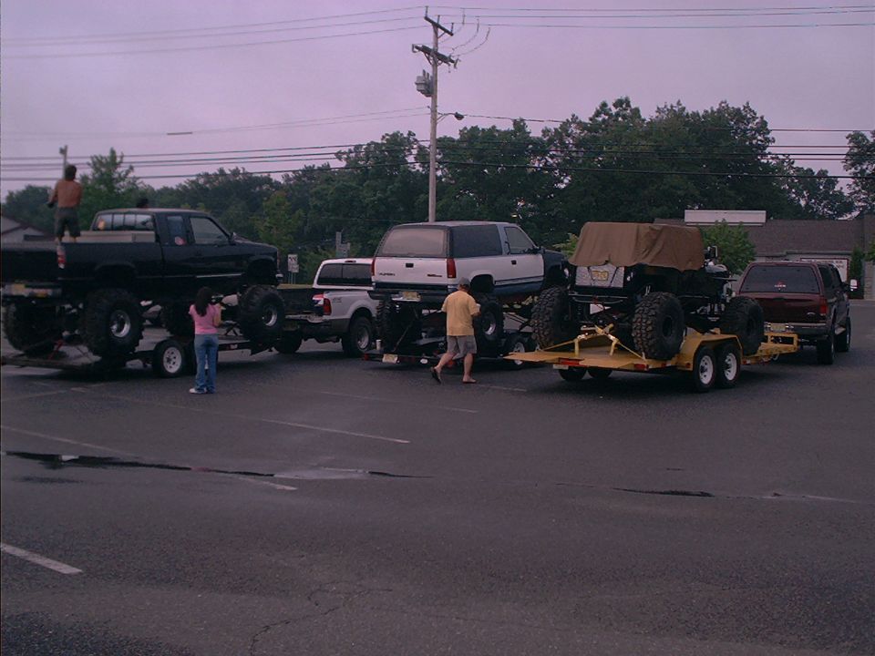 Four lifted vehicles on trailers, including a black pickup and a white SUV