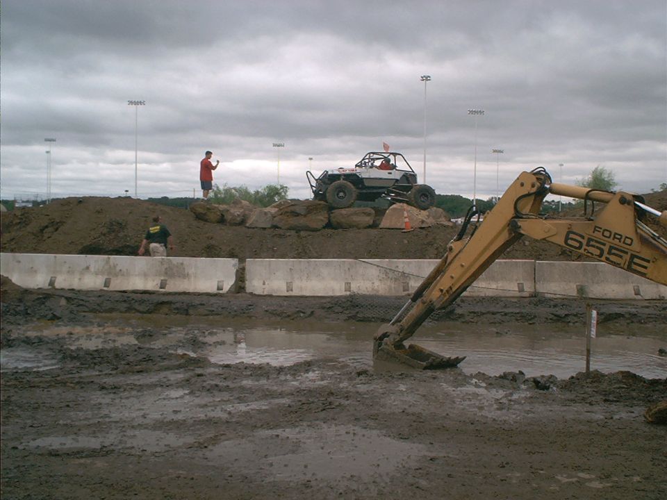 Off-road buggy on dirt mound with excavator in foreground mud pit