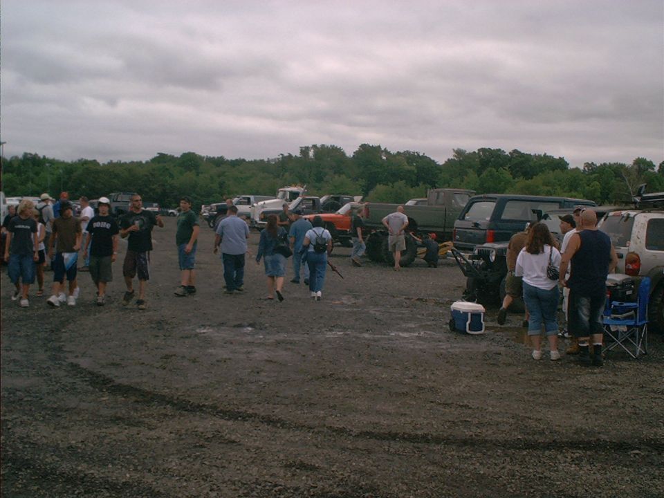 Group of people standing around in a gravel lot with many trucks and SUVs parked