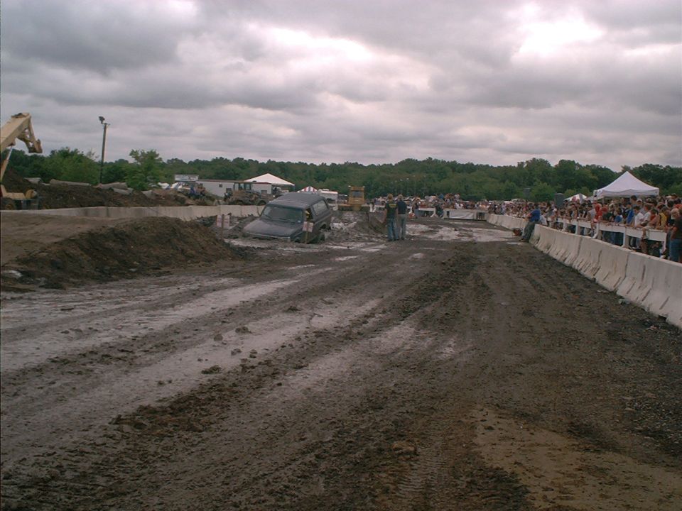 Dark SUV partially submerged in mud with spectators watching from behind barriers